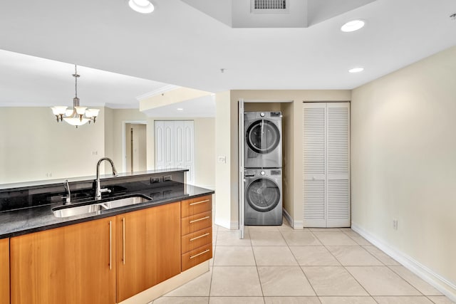 kitchen with pendant lighting, stacked washer and dryer, sink, ornamental molding, and a notable chandelier