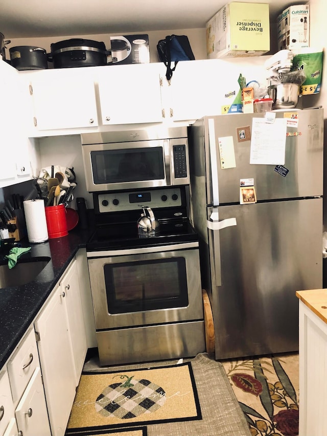 kitchen featuring stainless steel appliances, white cabinets, sink, and dark stone countertops