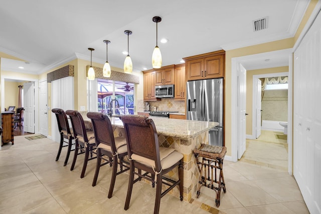 kitchen featuring light stone countertops, stainless steel appliances, an island with sink, decorative light fixtures, and a breakfast bar area