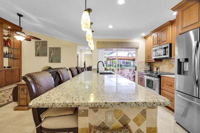 kitchen featuring pendant lighting, a breakfast bar, sink, light stone countertops, and appliances with stainless steel finishes