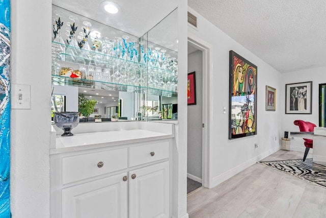 bar with a textured ceiling, white cabinetry, and light hardwood / wood-style floors