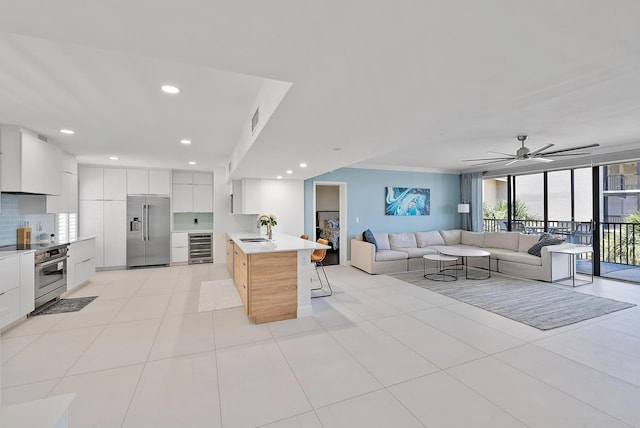 kitchen featuring sink, white cabinets, built in refrigerator, a breakfast bar area, and a center island with sink