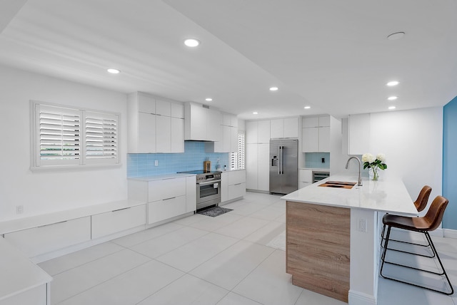 kitchen featuring a breakfast bar area, high end appliances, white cabinets, backsplash, and sink