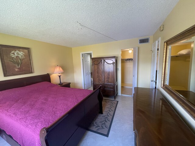 tiled bedroom with a walk in closet, a closet, and a textured ceiling