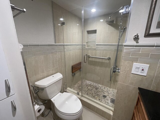 bathroom featuring tile walls, a shower with door, vanity, and toilet