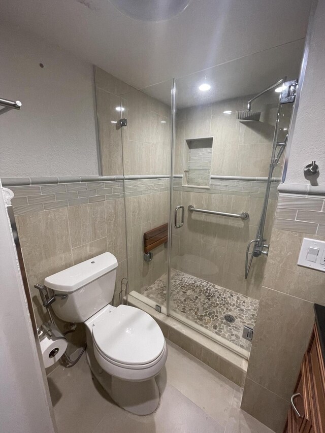 bathroom featuring walk in shower, tile floors, tile walls, vanity, and toilet