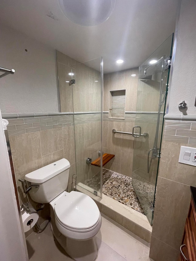 bathroom with tile walls, toilet, tile floors, a shower with shower door, and vanity