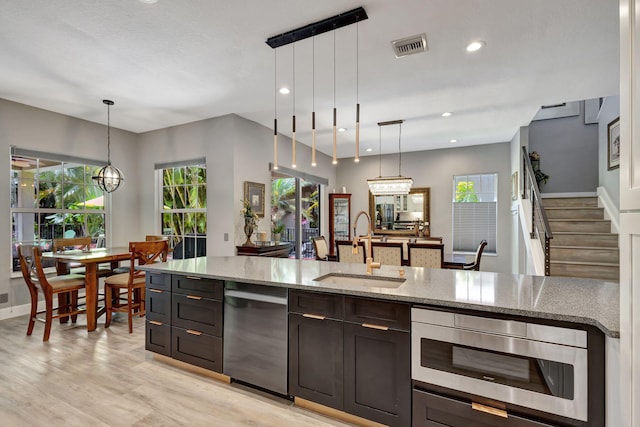 kitchen with stainless steel appliances, sink, light stone countertops, hanging light fixtures, and light wood-type flooring