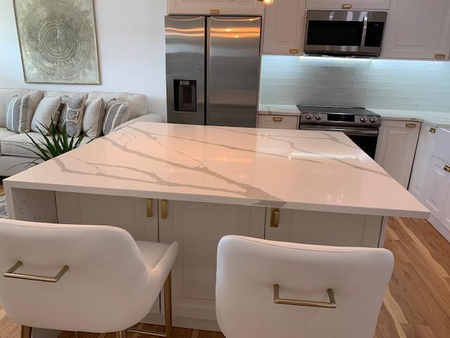 kitchen with white cabinets, light stone countertops, light hardwood / wood-style floors, a kitchen bar, and stainless steel appliances