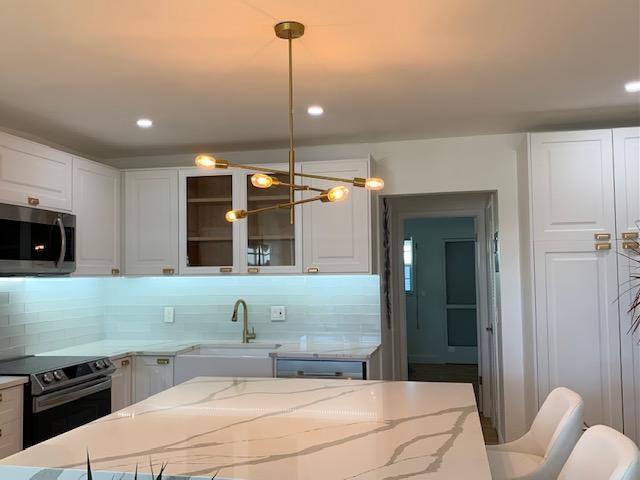 kitchen featuring sink, light stone counters, black electric range oven, pendant lighting, and white cabinets