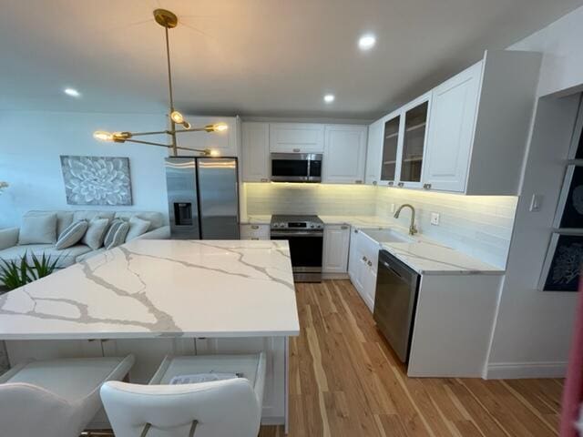 kitchen featuring light stone countertops, hanging light fixtures, white cabinets, and stainless steel appliances