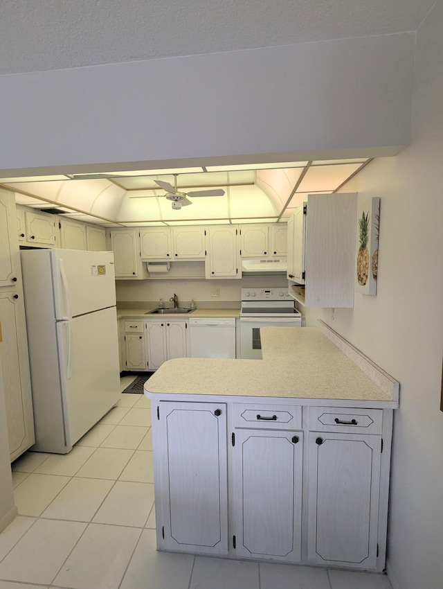 kitchen with a sink, white appliances, a peninsula, light countertops, and light tile patterned floors