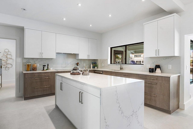 kitchen featuring backsplash, white cabinetry, a center island, light stone countertops, and sink