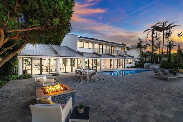 back house at dusk with a patio area and an outdoor living space with a fire pit