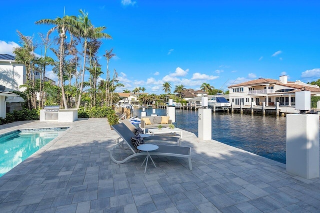 view of pool with a boat dock, a water view, a patio area, and an outdoor kitchen