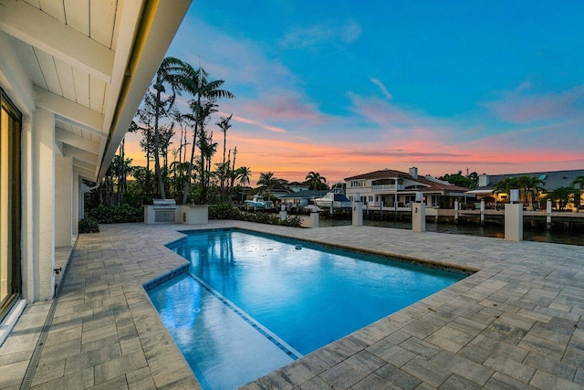 pool at dusk featuring a patio and exterior kitchen