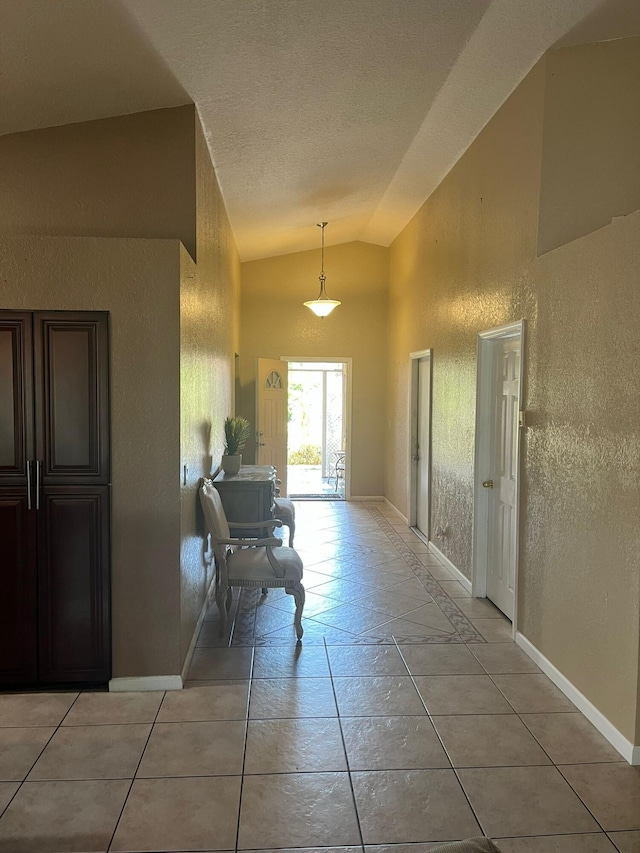 hallway featuring a textured ceiling, lofted ceiling, and light tile floors