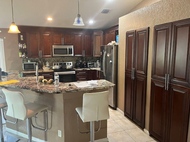 kitchen with tasteful backsplash, light tile flooring, pendant lighting, a breakfast bar area, and appliances with stainless steel finishes