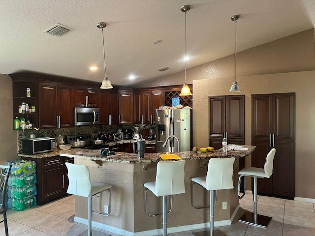 kitchen with tasteful backsplash, light tile floors, hanging light fixtures, lofted ceiling, and appliances with stainless steel finishes