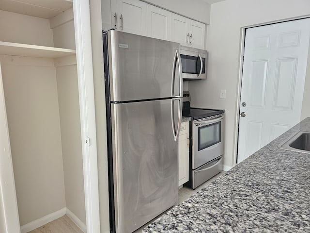 kitchen with appliances with stainless steel finishes, white cabinetry, and dark stone counters