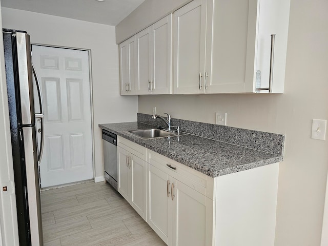 kitchen with stainless steel appliances, sink, white cabinetry, and dark stone counters