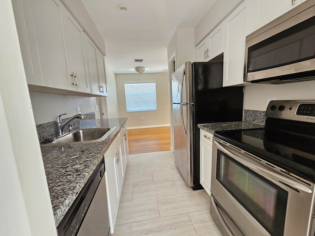 kitchen with stainless steel appliances, white cabinetry, dark stone countertops, sink, and light tile floors