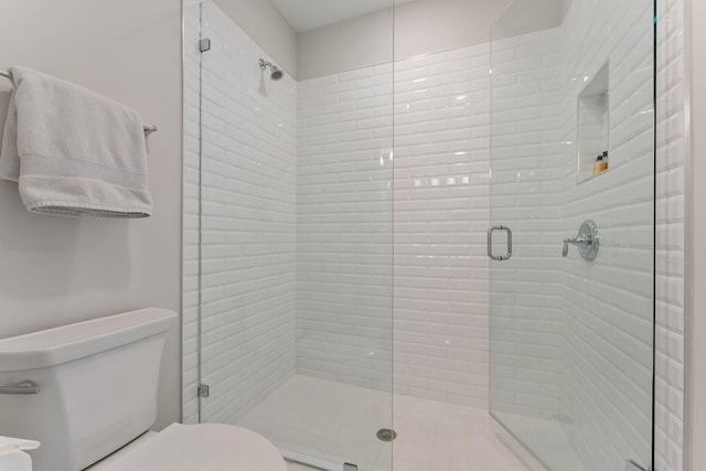 bathroom featuring a shower with door and toilet