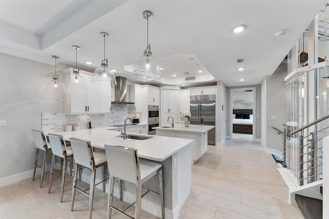 kitchen featuring white cabinets, wall chimney exhaust hood, a raised ceiling, and decorative light fixtures