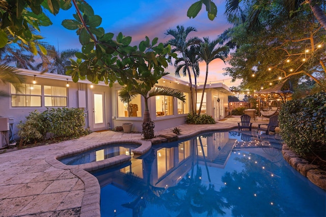 pool at dusk with an in ground hot tub and a patio