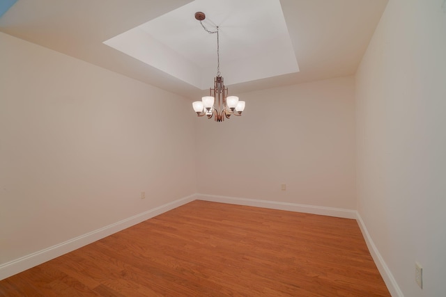 unfurnished room featuring a tray ceiling, an inviting chandelier, and hardwood / wood-style flooring