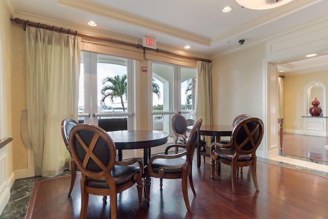 dining area featuring dark wood-type flooring, ornamental molding, and a raised ceiling