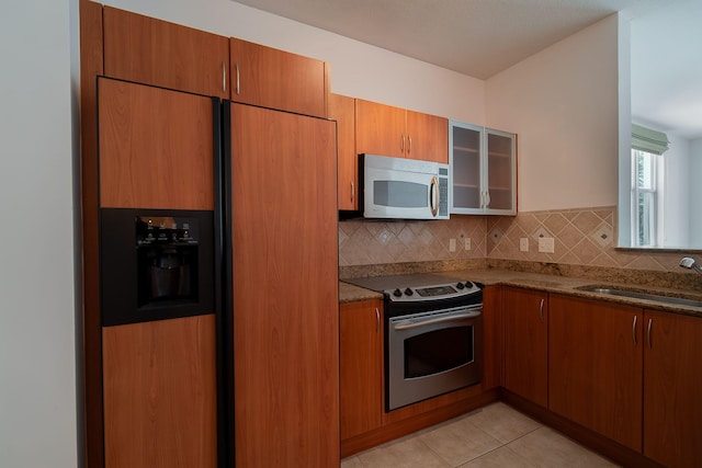 kitchen featuring dark stone countertops, appliances with stainless steel finishes, backsplash, sink, and light tile floors