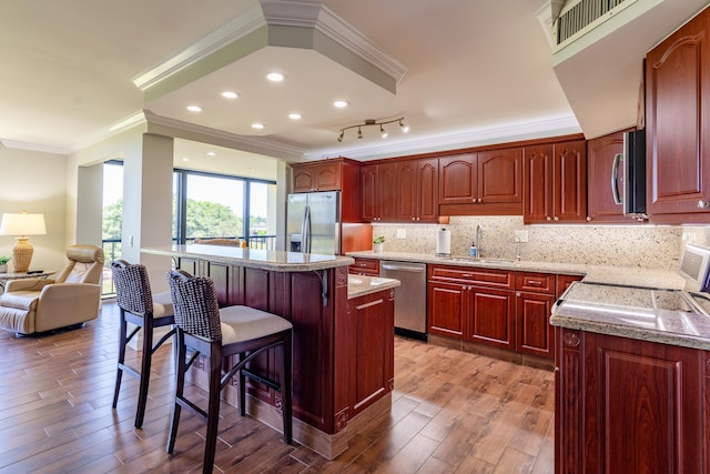 kitchen featuring light wood-type flooring, stainless steel appliances, crown molding, sink, and a breakfast bar area