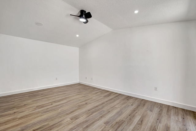 empty room with a textured ceiling, light hardwood / wood-style flooring, and vaulted ceiling