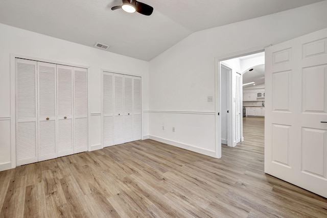 unfurnished bedroom featuring lofted ceiling, ceiling fan, light hardwood / wood-style flooring, and two closets