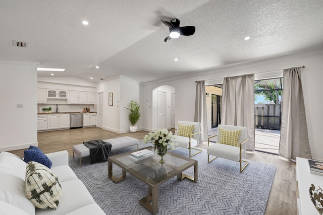 living room featuring a textured ceiling, crown molding, lofted ceiling, and light wood-type flooring