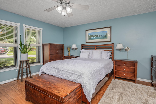 bedroom with ceiling fan, wood-type flooring, and a textured ceiling