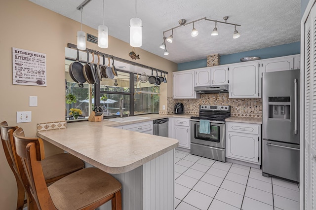 kitchen with kitchen peninsula, backsplash, white cabinets, pendant lighting, and appliances with stainless steel finishes