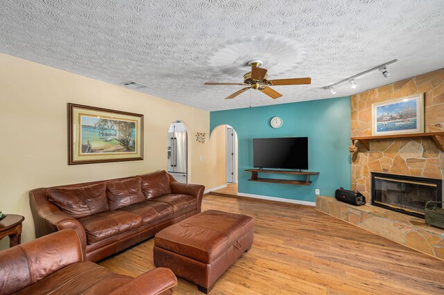 living room featuring rail lighting, light wood-type flooring, a textured ceiling, a fireplace, and ceiling fan