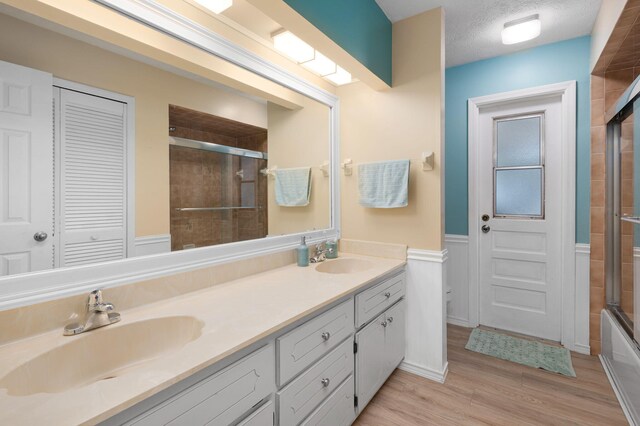 bathroom with vanity, a textured ceiling, enclosed tub / shower combo, and hardwood / wood-style flooring