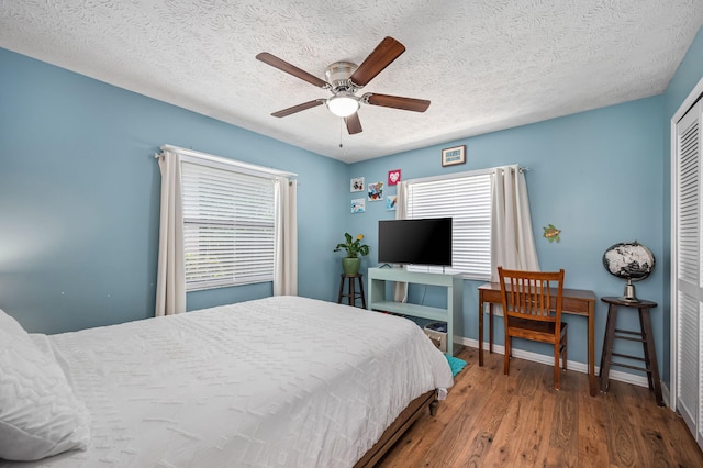 bedroom with ceiling fan, a textured ceiling, multiple windows, and hardwood / wood-style floors