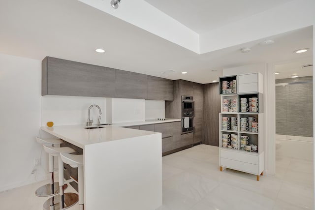 kitchen featuring a kitchen bar, sink, kitchen peninsula, stainless steel double oven, and black electric stovetop