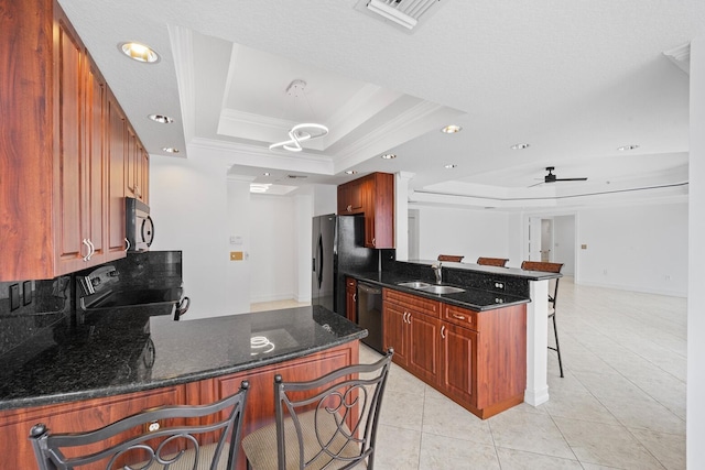 kitchen featuring kitchen peninsula, a tray ceiling, sink, black appliances, and a breakfast bar area