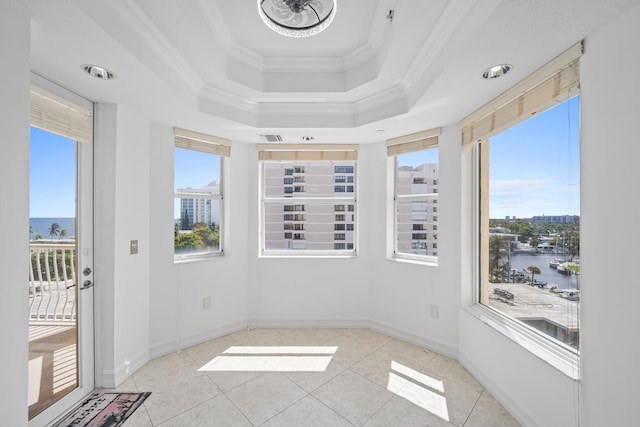 empty room featuring a water view, a tray ceiling, crown molding, and light tile patterned flooring