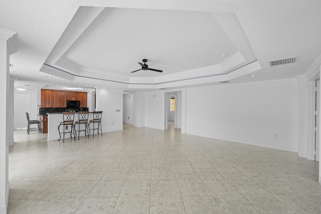 unfurnished living room with a tray ceiling, ceiling fan, crown molding, and light tile patterned flooring