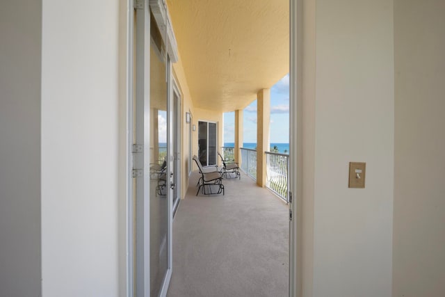 hallway with a water view, light colored carpet, a textured ceiling, and a wall of windows