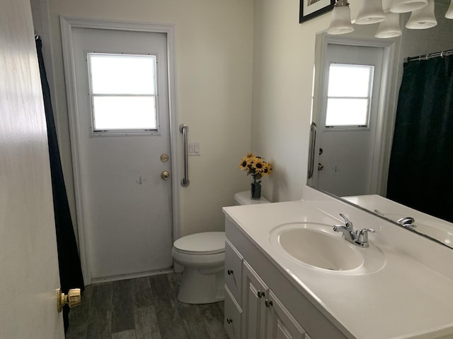 bathroom with wood-type flooring, vanity, toilet, and a healthy amount of sunlight