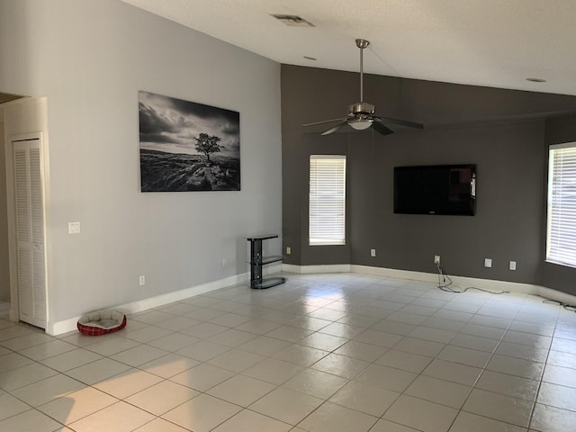 unfurnished living room with ceiling fan, plenty of natural light, light tile patterned floors, and vaulted ceiling