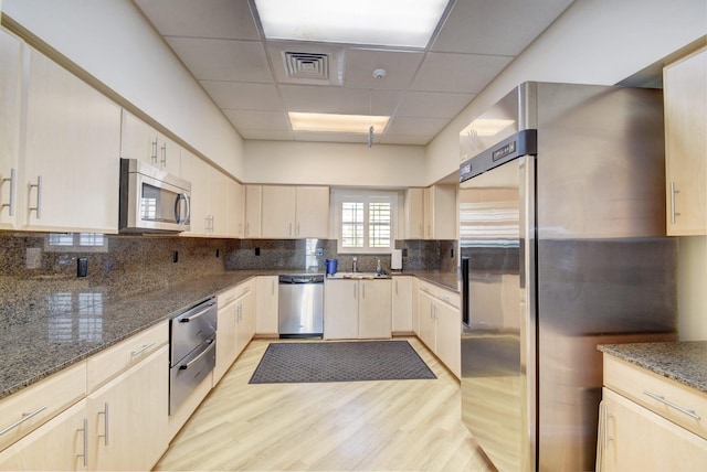 kitchen featuring dark stone counters, a drop ceiling, light hardwood / wood-style floors, and appliances with stainless steel finishes