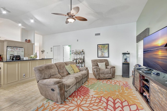 living room featuring ceiling fan, light wood-type flooring, a textured ceiling, and vaulted ceiling